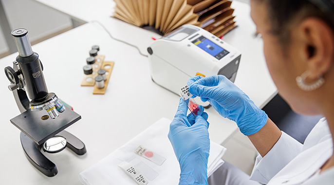 Frau mit Handschuhen klebt ein Etikett auf eine Blutprobe
